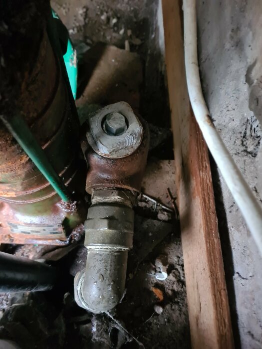 Närbild av rörledningskoppling och del av Grundfos ejektorpump i ett gammalt installationsutrymme med rost och damm.