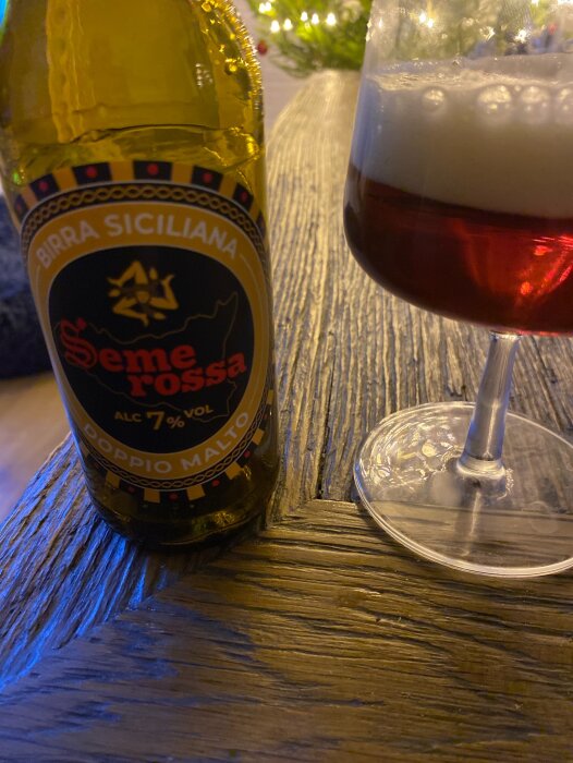 Flaska med Birra Siciliana Seme Rossa Doppio Malto och glas med skummande öl på träbord.