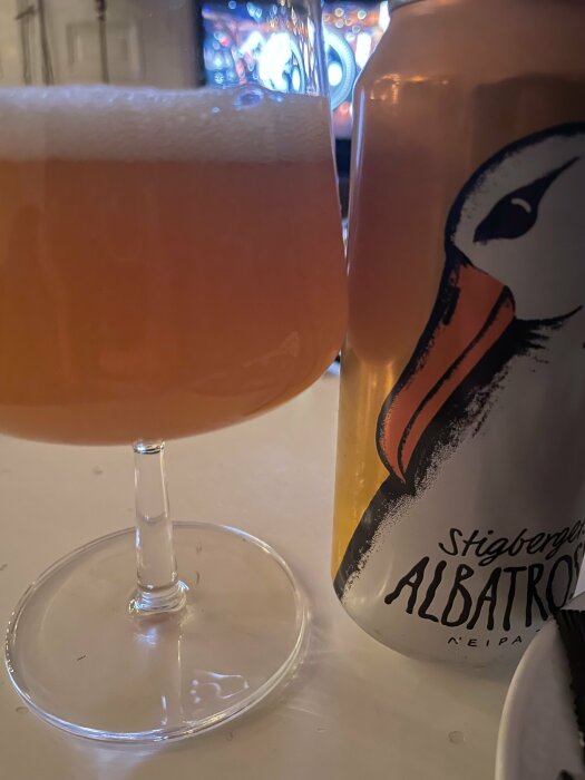 Ett glas öl bredvid en burk Stigbergets Albatross NEIPA på ett bord.