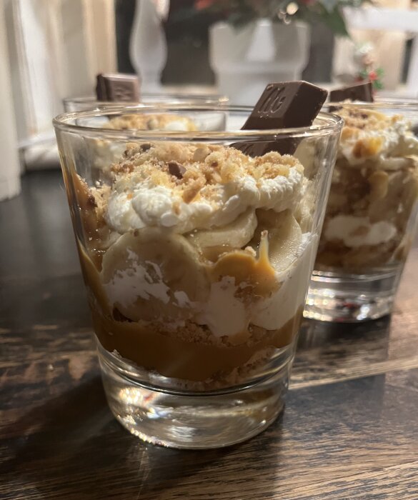 Dekonstruerad banoffeepaj i glas med grädde, skivad banan, karamell och kexkross, dekorerad med choklad på toppen.