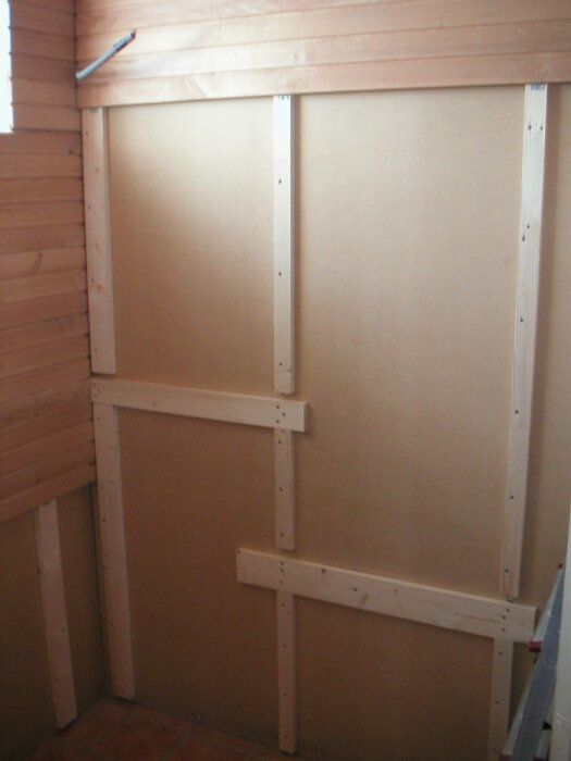 Vägg med masonit och träreglar i en källare för en bastu, förstärkningar för lavar infällda i reglarna.