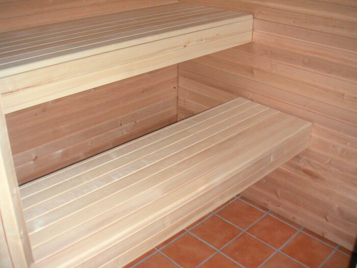 Bilden visar sittbänkar i en bastu med avtagbara träramar monterade i väggen för enkel rengöring.