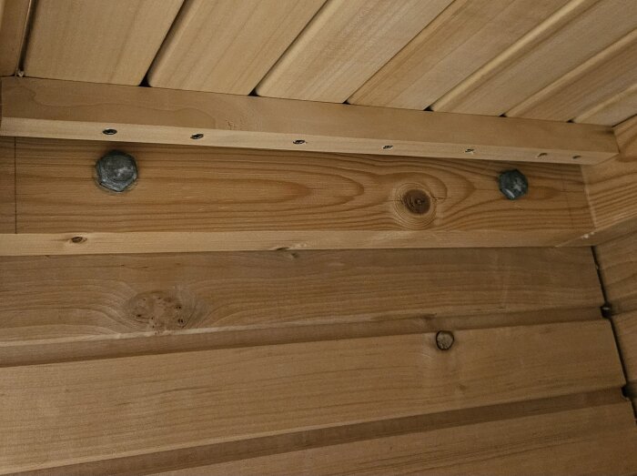 Träram fastskruvad i liggande träpanel med stående läkt som stöd, visas genom skruvar och bultar på ramen.