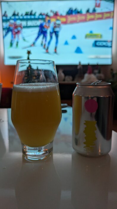 Glas med öl och en burk Omnipollo Fatamorgana, bakgrund med skidtävling på TV.