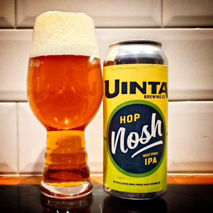 Ett glas med skummande öl bredvid en burk Uinta Brewing Co. Hop Nosh West Coast IPA.