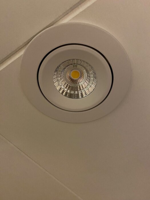 Inbyggd takspotlight med rund vit ram och glaslins, fotograferad rakt underifrån.