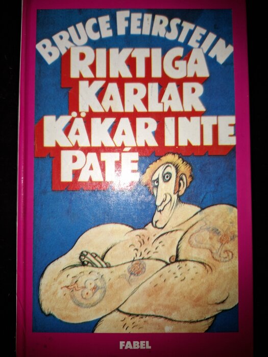 Bokomslag med titeln "Riktiga karlar käkar inte pâté" av Bruce Feirstein, visar en muskulös man med tatueringar.