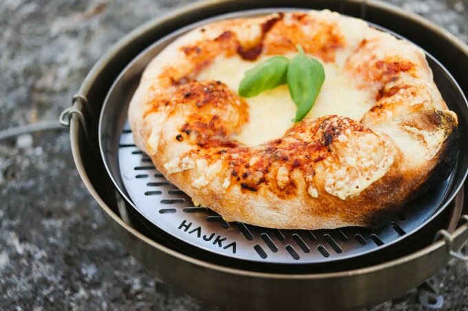 Pizza i Hajka bärbar ugn på en Trangia, toppad med basilika, fotograferad utomhus.