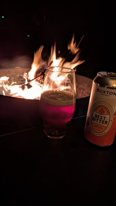 Glas med öl och ölburk framför brinnande eld.