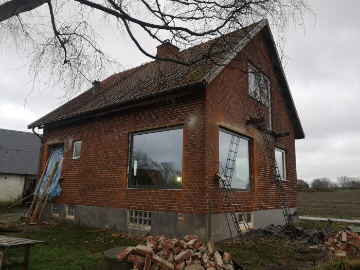 Tegelhus med nyputsade fönster, byggställning och byggmaterial vid foten av väggen. Tegelbitar på marken längs husets kortsida.