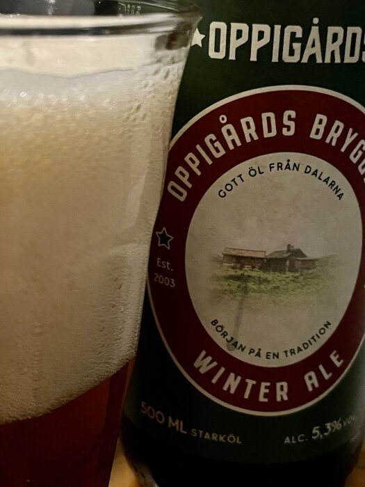 Glas med skummande öl bredvid en flaska Oppigårds Bryggeri Winter Ale, etikett synlig med "Gott öl från Dalarna".