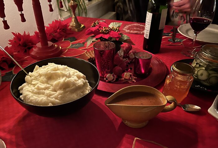 Thanksgiving-måltid på röd duk med skål potatismos, såsskål, inlagd gurka och äppelgelé, omgiven av röda dekorativa föremål.