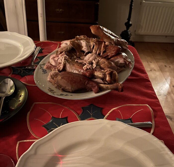 En tallrik med skivad och stekt kalkon på ett julbord med röd duk, omgiven av bestick och en tallrik.
