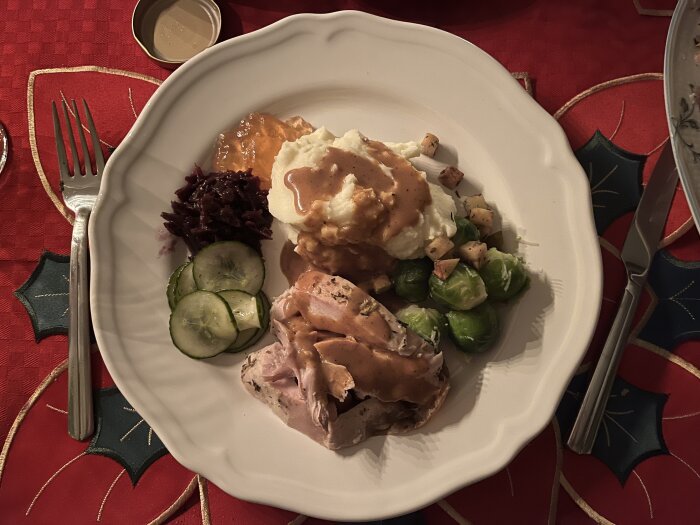 Tallrik med skivad kalkon, potatismos, brunsås, brysselkål, inlagd gurka, rödkål och äppelgelé på röd julduk.