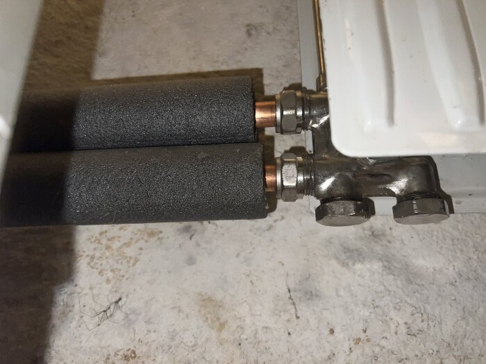 Radiatorkoppel med två isolerade rör anslutna till element och två muttrar längst ner.