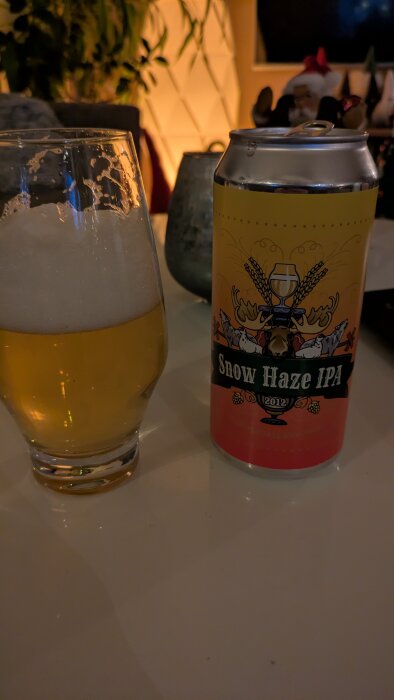 En burk Snow Haze IPA och ett glas öl på ett bord, med varm belysning i bakgrunden.