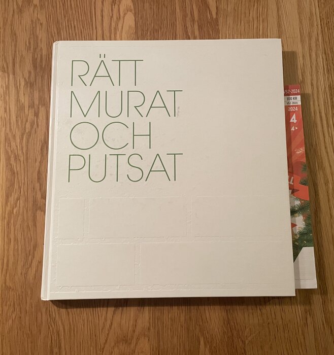 Omslag av boken "Rätt murat och putsat" som ligger på ett träbord.