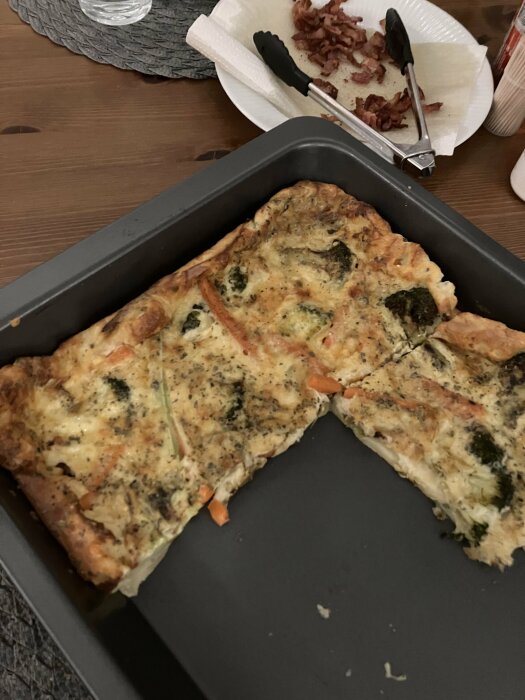 Ugnspannkaka med broccoli, morot och riven ost i form, med bacon på en tallrik bredvid.