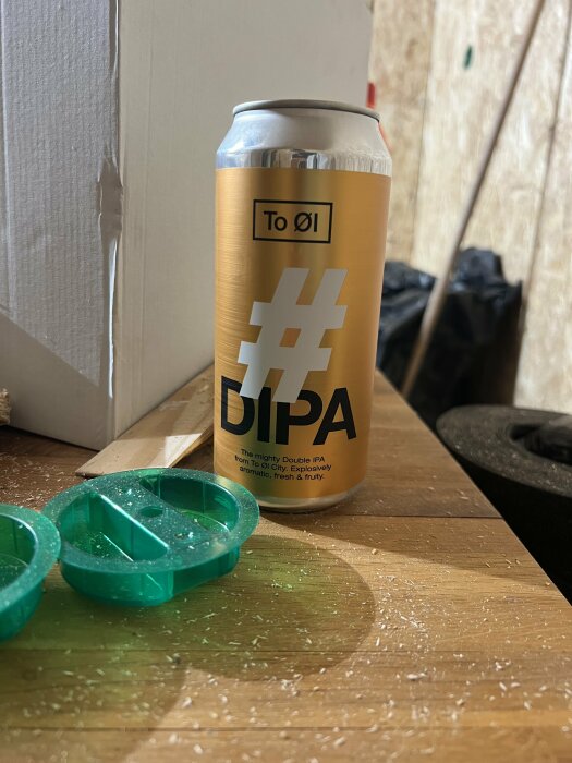 Burk med To Øl Double IPA öl på en bänk med sågspån och gröna plastverktyg.