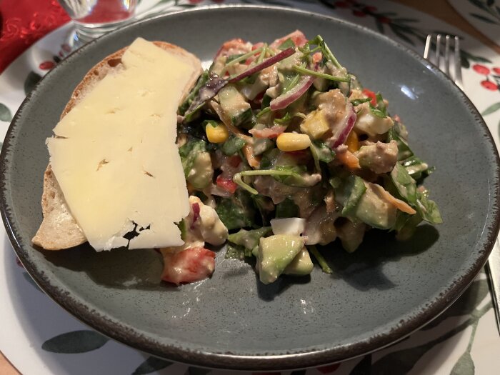 Tonfisksallad med grönsaker och bitar av bröd toppat med ost på tallrik.