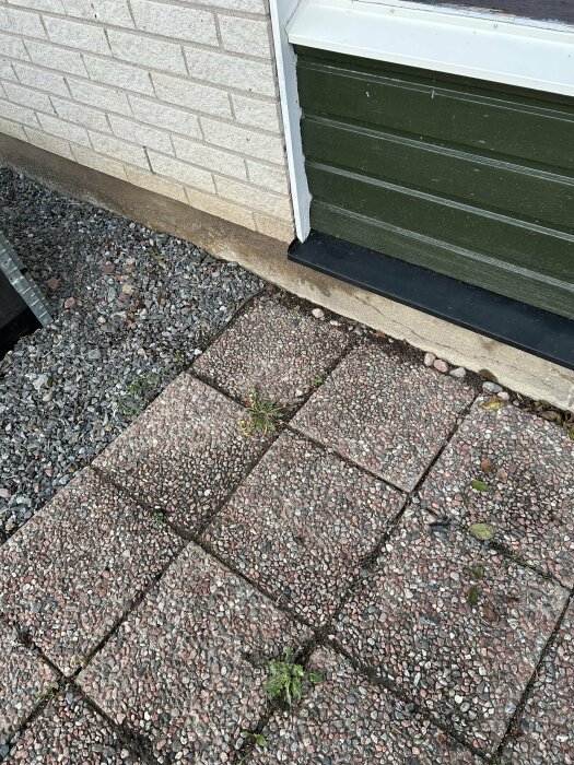 Husgrund med fuktig grusdel och torr plattlagd yta som gränsar till väggen.