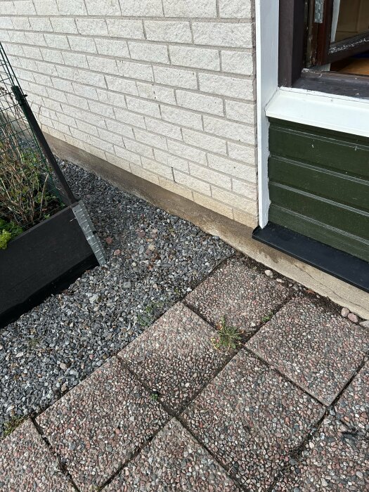 Bilden visar en husfasad med grus och marksten. Gruset verkar fuktigt medan markstenarna är torra.