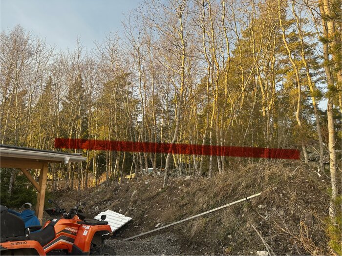 Vy över skogskant och sluttande mark från en carport, med en röd linje som markerar möjlig plats för en planerad ramp.