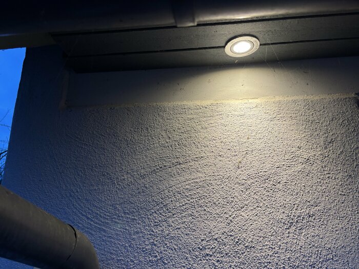 Närbild på en vägg med en spotlight ovanför. Väggen är grovputsad och ljusgrå, spotlighten lyser upp ett område av väggen.