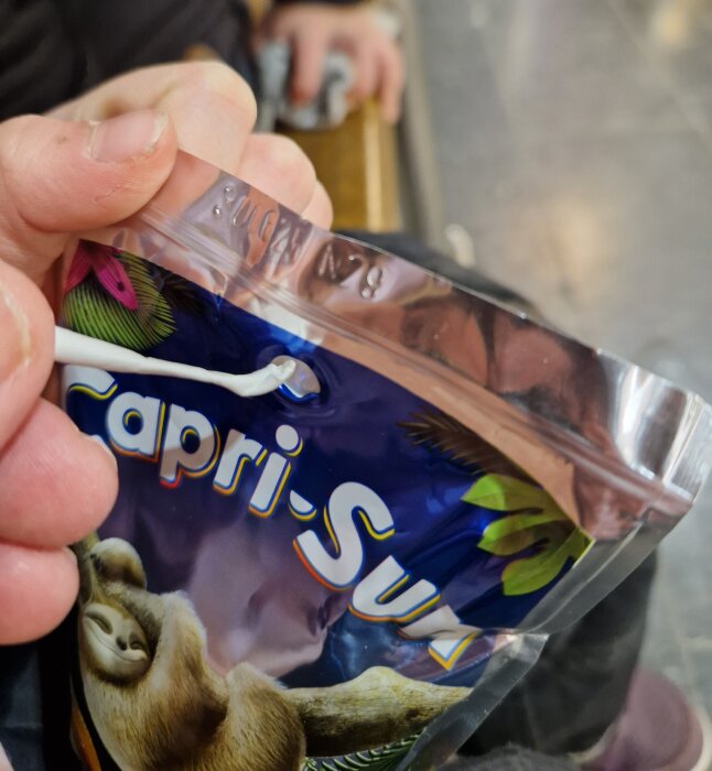 Närbild på hand som håller Capri-Sun med ett böjt papperssugrör instucket i förpackningen.