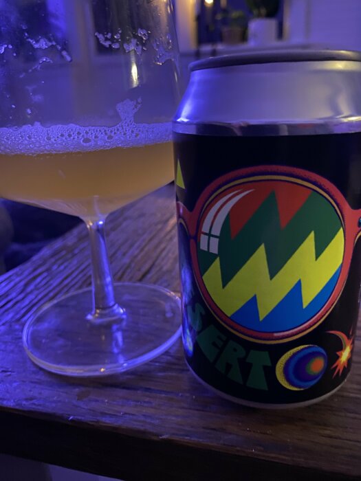 En Omnipollo-ölburk och ett glas med halvdrucken öl på ett bord i kvällsbelysning.