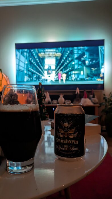 Ett glas och en burk med Snöstorm Imperial Stout från Sälens Fjällbryggeri på ett bord. En TV visar en film i bakgrunden.