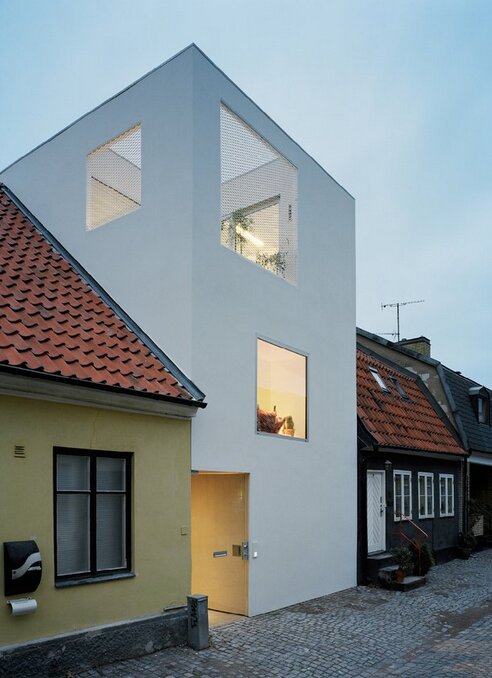 Modernt vitt townhouse i Landskrona med stora fönster, beläget mellan två äldre hus.