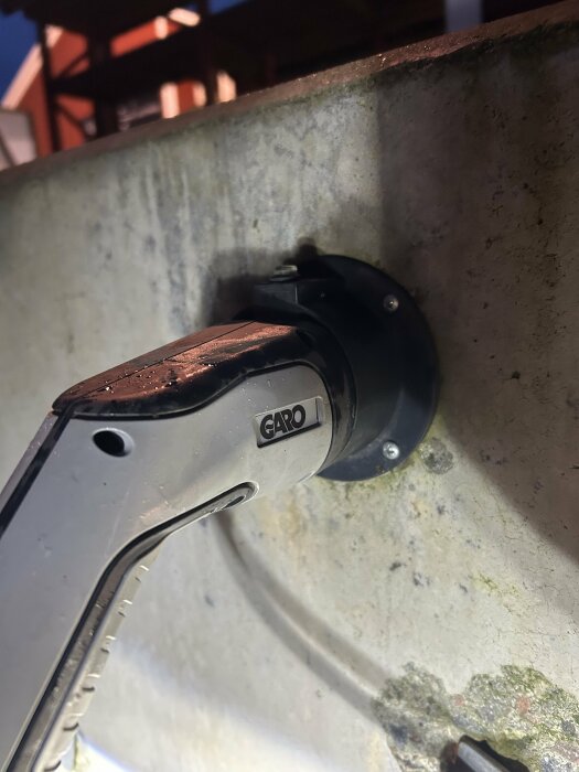 Laddkabelhållare monterad på en vägg med märkning "Garo", knapp för att lossa kabeln ovanpå.