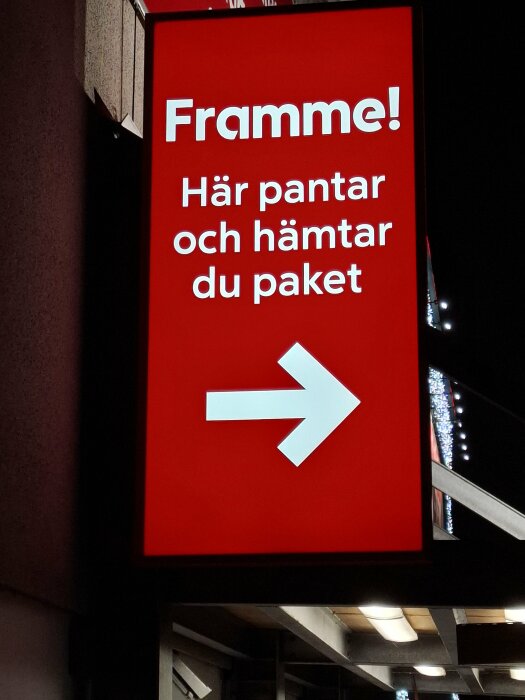 Röd skylt vid ICA som visar texten "Framme! Här pantar och hämtar du paket" med en vit pil som pekar åt höger.