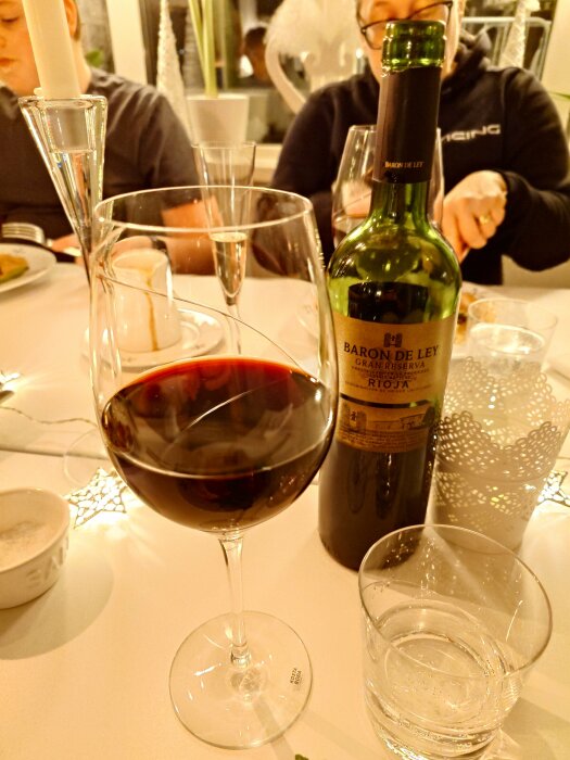 Ett glas rött vin och en flaska Baron de Ley Rioja på ett dukat bord.