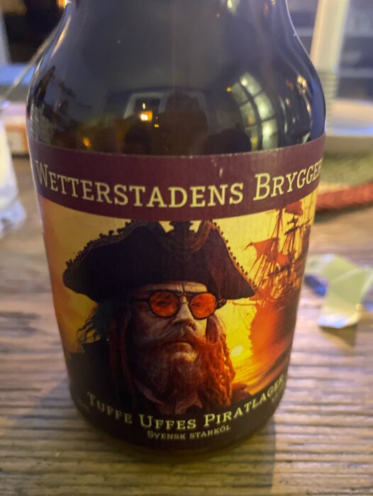 Flaska med etikett Wetterstadens bryggeri, Tuffe Uffes Piratlager, illustrerad med en piratfigur mot en solnedgång.