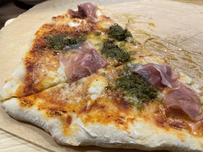 Hemlagad pizza med pesto och prosciutto på bakplåtspapper.