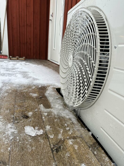 Luftvärmepump på altan vid entré, täckt med is som bildats vid nollgradig temperatur, utan något takskydd ovanför fläkten.