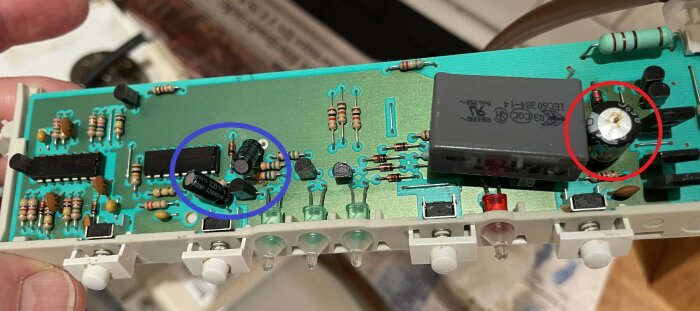 Kretskort med komponenter, två kondensatorer i blå ring, märkta 63V 10 mikrofarad, och en kondensator i röd ring, märkt 1000 mikrofarad 16V.