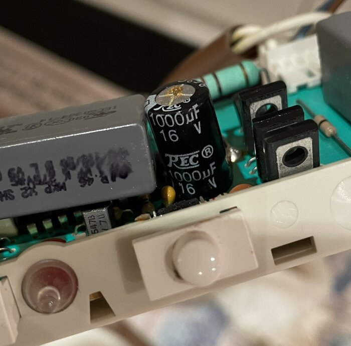 Närbild av kretskort i en köksfläkt, med fokus på elektrolytisk kondensator märkt 1000μF 16V monterad vertikalt på en grön kretskortsyta.