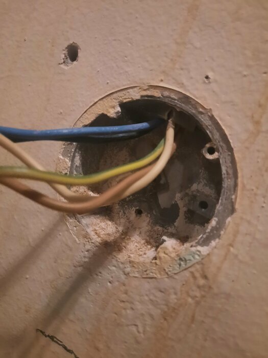 Gammal kopplingsdosa i gjuten vägg med synliga elektriska kablar, förberedd för installation av ett infällt perilexuttag.