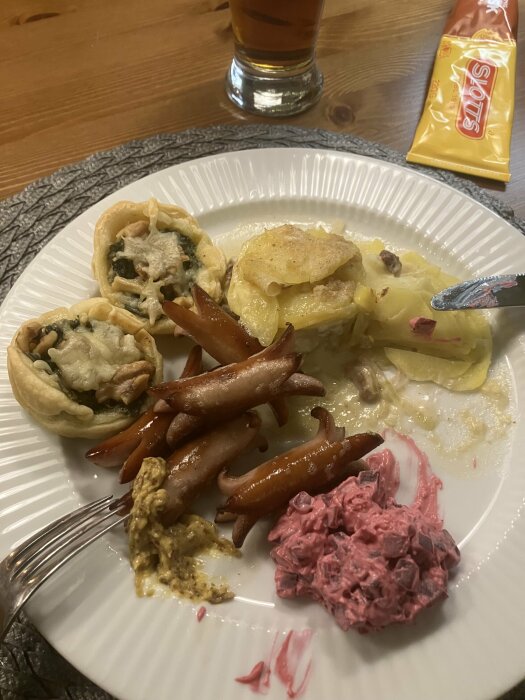 Tallrik med Janssons frestelse, prinskorv, grönkål i smördeg, rödbetssallad och julkorv på ett bord.