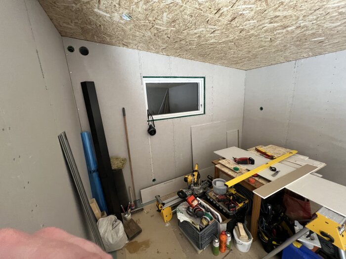 Nyrenoverat rum med väggar av gipsskivor, verktyg och material. Arbetsyta med olika verktyg och byggutrustning syns i förgrunden.
