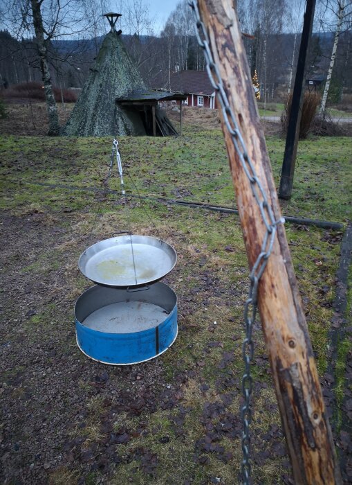 Muurikka upphängd i trebening av störar, använd för att steka hamburgare. Kedja och wire för att justera höjden ovanför marken.