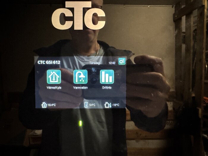 CTC GSi 612-panel med temperaturinställningar, spegelbild av person som tar foto. Temperaturen inomhus är 19,4°C och utomhus -18°C.
