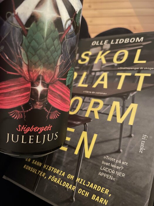 En ölburk från Stigbergets Juleljus bredvid boken "Skolplattformshelvetet" av Olle Lidbom.