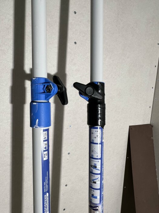 Två stöttor med blå plasthöljen och vred, den ena lagad med svart eltejp. Används vid byggprojekt för att stödja takplattor.