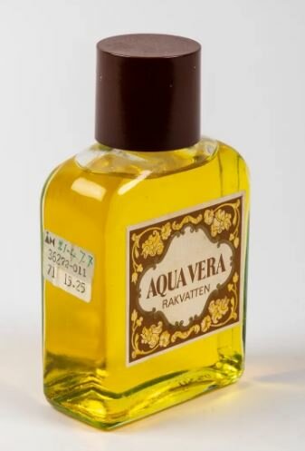 Flaska med rakvatten av märket Aqua Vera, med gul vätska och brun kork.