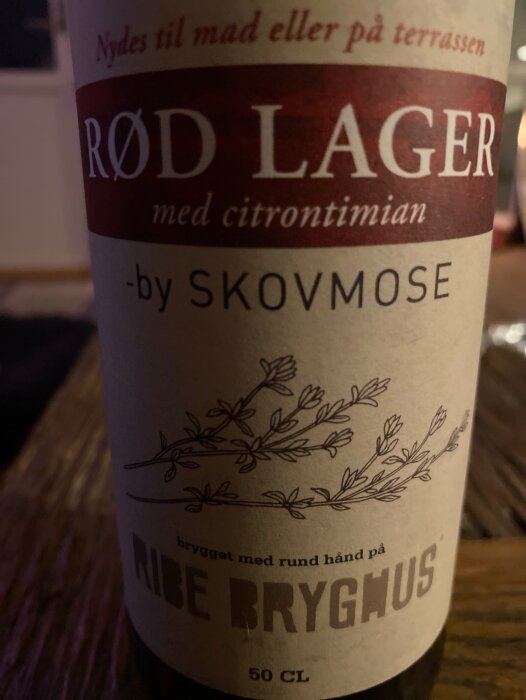 Flaska med dansk öl, Rød Lager med citron och timjan från Ribe Bryghus, etikett med växtmotiv och text på danska.