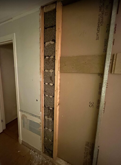 Öppen sektion av en innervägg med lecablock synliga mellan träreglar, i samband med renovering och eventuell påverkan på eldstad.